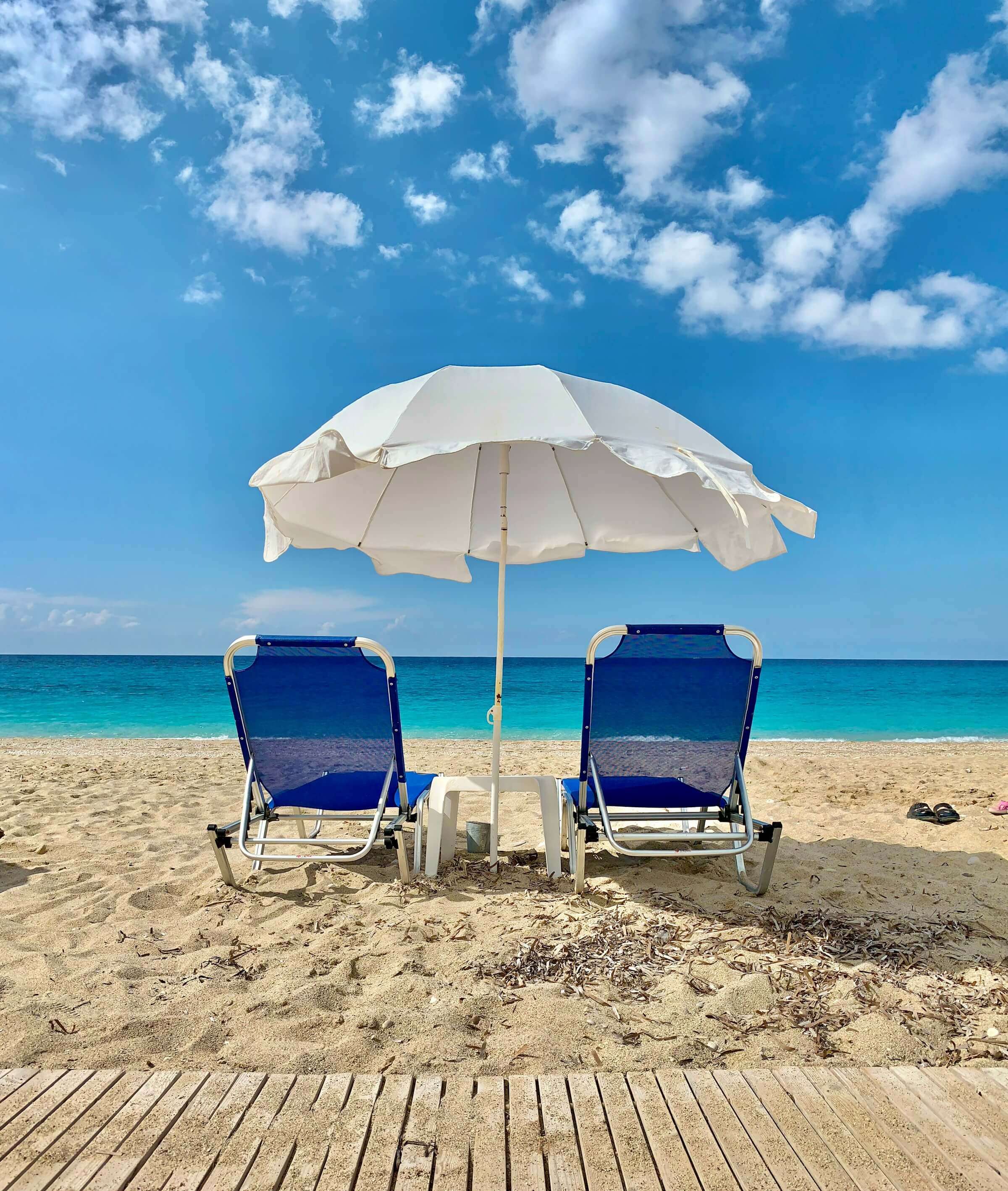 Two sun loungers under a white parasol on a turquoise coastline